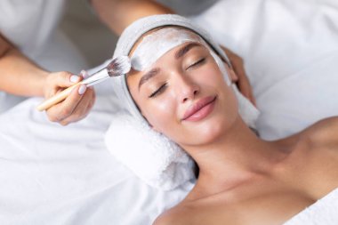 Estetik, modern sağlık merkezindeki genç bir kadının yüzüne beyaz kilden bir maske takıyor. Güzellik ve estetik kavramlar