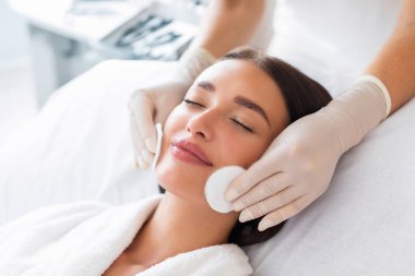 Pamuk pedlerle cilt temizleme. Lüks kaplıca salonunda güzellik uzmanları tarafından yüz bakımı gören genç bir kadın.