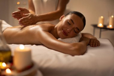 Doğu kaplıcasında sırt masajı yaptıran barışçıl genç Avrupalı bayan mumlarla süslenmiş bir oda ve çeşitli aromaterapi aletleri.