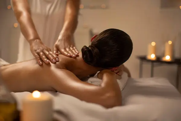 stock image Relaxed woman lying on massage table while massage therapist massages her back, applying pressure to release tension in the woman muscles