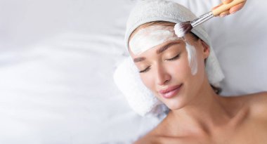 Güzeller güzeli genç bir kadın kozmetolog randevusunda güzellik salonunda uzanırken yüz maskesi takmaktan zevk alır.