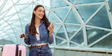 Seyahat başvurusu. Havaalanında ya da tren istasyonunda bavulla beklerken akıllı telefon kullanan bir kadın biletleri telefonla kontrol ediyor.