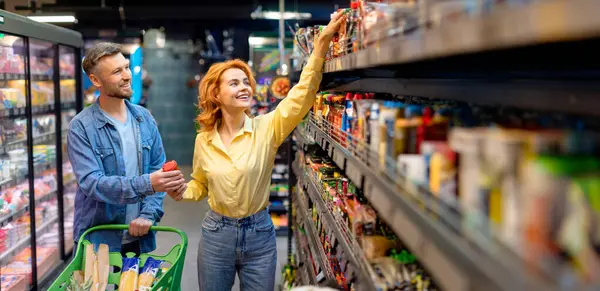 Hipermarkette alışveriş yapan, yiyecek seçen ve alan, süpermarkette tramvay arabasıyla yürüyen eşler.