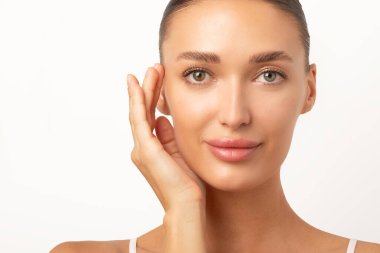 Estetik prosedür konsepti. Genç Avrupalı kadın portresi parlayan tene dokunuyor, beyaz stüdyo arka planı