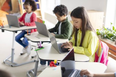 İlkokulun bilgisayar sınıfında dizüstü bilgisayar kullanan çeşitli çocuklar, bilgisayar bilimi öğreniyorlar.