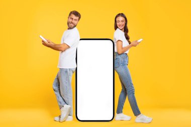 Avrupalı eşler dev akıllı telefonun yanında boş ekranlı, uygulamayı veya web sitesini destekleyen, sarı stüdyo geçmişi olan
