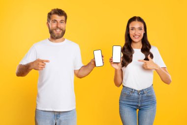 Uygulamayı öneriyoruz. Mutlu Avrupalı çift, cihazlara işaret ederek boş ekranlı iki cep telefonunu tutuyor ve gösteriyor.