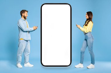 Avrupalı erkek ve kadın büyük bir cep telefonuna doğru yürüyorlar. Beyaz ekranları boş ve telefonlarını kullanıyorlar. Birbirlerine gülümsüyorlar.