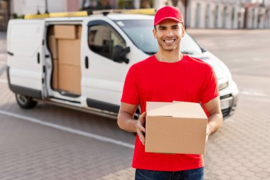 Kurye servisi ya da stok. Karton paketli gülen teslimatçı dışarıda müşteri bekliyor.