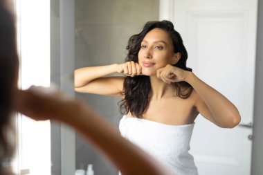 Banyoda lenfatik drenaj yüz masajı yapan bir kadın, banyoda ev içi cilt bakımı yapan bir kadın.