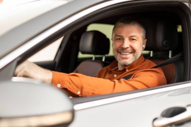 Gülümseyen Avrupalı orta yaşlı işadamı sürücü koltuğunda oturuyor, şehirde el ele yürüyor ve kameraya gülümsüyor.