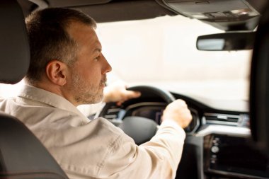 Orta yaşlı bir sürücü otomobilde oturuyor, yol kenarına bakıyor, arkadan bakıyor. Trafik ve ulaşım kavramı