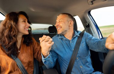 Ön koltukta oturan mutlu Avrupalı eşler ve sürücüler arabada oturup el ele tutuşuyor ve birbirlerine gülümsüyorlar.