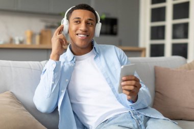 Rahat Afro-Amerikalı adam akıllı telefondan müzik dinliyor, kablosuz kulaklıkla favori şarkıları dinliyor ve arkadaşlarıyla mesajlaşıyor.