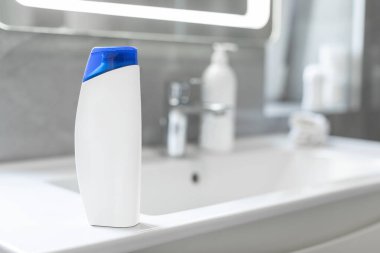 Bir şişe şampuan ve banyo tezgahındaki lavabo, boş alan ve seçici bir odak noktası.