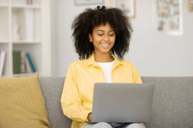 Evdeki kanepede oturan neşeli siyah bayan, dizüstü bilgisayar kullanıyor, arkadaşlarıyla sohbet ediyor, blog okuyor ya da uzaktan ders çalışıyor, uzayı kopyalıyor.