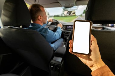 Taksi servisi başvurusu. Kadın yolcu elinde boş ekranlı akıllı telefon, şoför araba kullanırken kadın arka koltukta oturuyor. Model