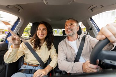 Mutlu Avrupalı eşler birlikte araba kullanıyor, bir şeyi parmağıyla işaret ediyor, kocası sürücü koltuğunda oturuyor, birlikte gezmekten zevk alıyor.