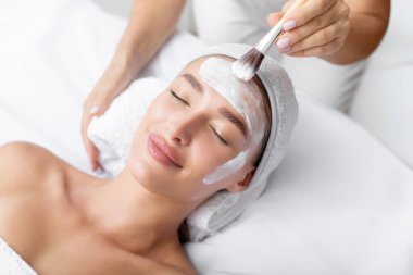 Güzel, rahat, genç bir kadın aljinat kozmetik maske takmaktan zevk alıyor. Kapalı gözlerle uzanıyor ve kaplıca merkezinde, yukarıdan çekimin keyfini çıkarıyor.