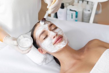Güzellik tedavisi. Profesyonel güzellik uzmanı kaplıca salonundaki bayana kilden maske takıyor. Kadın yüz bakımından hoşlanıyor.