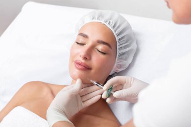 Profesyonel kozmetik uzmanı, kadının çenesinde yağ yakmak için lipolitik enjeksiyon yapıyor. Güzellik salonunda güzellik prosedürleri uyguluyor. Kozmetoloji kavramı