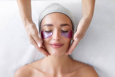 Kozmetolog kabinesinde cilt bakımı sırasında yalan söyleyen göz altında besleyici bantları olan bir kadın yaşlanma karşıtı cilt bakımı görüyor.