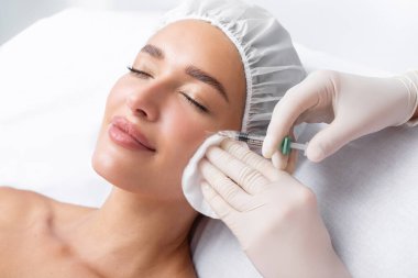 Beautiful relaxed woman at beautician cabinet receiving anti wrinkle injections on cheekbones, lying with closed eyes in beauty salon clipart