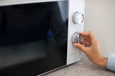 Mutfakta mikrodalga fırını ayarlayan kadın ısıtma zamanlayıcısı ayarlıyor, yakın çekim.