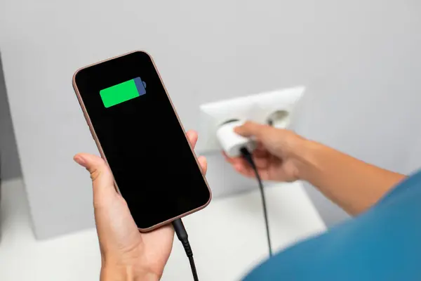 stock image Lady holding cellphone while putting on charging into wall outlet. Charging phone with regular charger concept