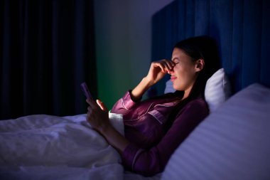 Geceleri cep telefonu kullanırken göz ağrısı çeken genç bir kadın. Uykusuzluktan muzdarip olarak yatakta yatıyor.