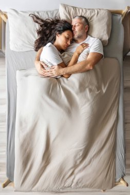 Sevgili eşler kucaklaşarak yatar, battaniyenin altında yatar, yatay çekimde üstten çekilir.
