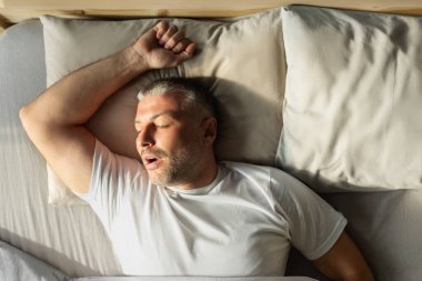 Yakışıklı orta yaşlı bir adamın evde dinlenmesi, kolları başının arkasında uzanması, rahat bir yatakta uyuması.