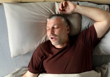 Middle aged man sleeping and snoring, lying with closed eyes in comfortable bed in bedroom at home, above view. Male sleep, recreation and wellness clipart