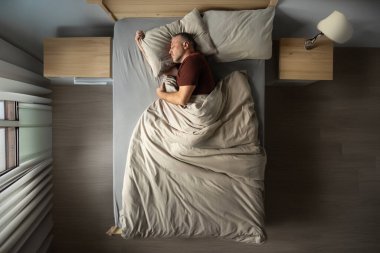 Pijamalı, yakışıklı, orta yaşlı bir adamın evde dinlenmesi, rahat bir yatakta yatması, fotokopi odası, uzun bir çekim.