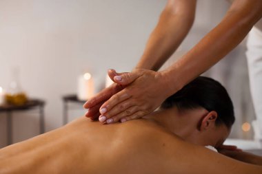 Profesyonel masör, arka planda aroma mumları olan sakin bir spa salonunda kadın vücuduna masaj yapıyor.