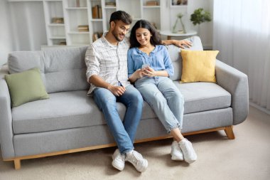 Hintli çift cep telefonlarını birlikte kullanıyor, rahat bir evde kanepede oturuyor, internette sörf yapıyor ya da arkadaşlarıyla sohbet ediyor. Modern, dijital bağlantılı yaşam tarzı