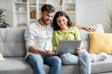Evdeki koltukta oturan mutlu Hintli çifti sevmek, kucaklaşmak, dizüstü bilgisayar kullanmak, genç adam ve kadının internetten film izlemesi, uzayı kopyalamak.