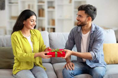 Romantik hediye. Sevgi dolu Hintli bir adam karısına ambalaj kutusu veriyor, yıldönümünü ya da doğum gününü kutluyor, evdeki kanepede oturuyor.