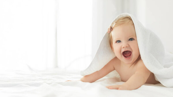 Уход за детьми и гигиена. Красивая девочка смеется, глядя на камеру, лежащую в постели после ванны под полотенцем, панорама с бесплатным пространством, баннер