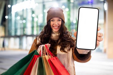 Elinde boş cep telefonu ve alışveriş poşetleri olan mutlu bir kadın. Mevsimlik kış satışları ve Xmas teklifleri içeren bir uygulama öneriyor.