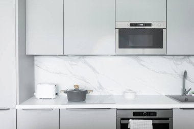 Tekniği olan modern mutfak mobilyaları, açık gri dolaplar, beyaz atölye ve beton duvar. Gri ve beyaz renkli mutfak.