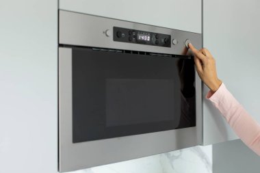 Mutfakta mikrodalga fırın kullanan ve açmak için düğmeye basan kadın, yakın çekim.