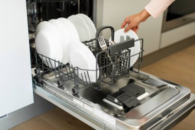 Female hand unloading dishwasher with tableware, washing kitchen appliances. Concept of modern technologies in the kitchen clipart