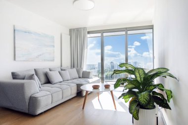 Beyaz ve gri mobilyaların, yumuşak aksanların ve bereketli yeşilliğin yer aldığı rahat ve aydınlık oturma odası davetkar bir atmosfer yaratıyor.