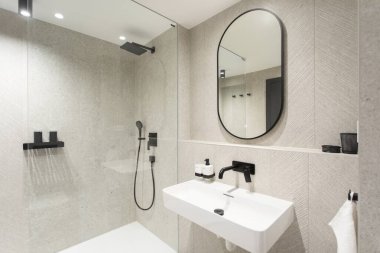 Beyaz lavabo, oval ayna, beyaz küvet ve siyah musluklar ile bej renkli modern banyo tasarımı