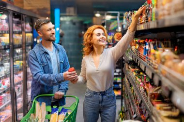 Hipermarkette alışveriş yapan, yiyecek seçen ve alan, süpermarkette tramvay arabasıyla yürüyen eşler.