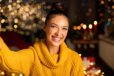Sevimli mutlu Avrupalı bayan selfie çekerken gülümsüyor ya da evde ışıklarla süslenmiş video davetiyesi kaydediyor.