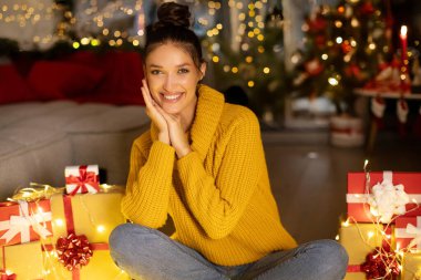 Noel ağacının önündeki süslü odada poz veren ve kameraya bakıp gülümseyen aşırı mutlu Avrupalı kadın portresi.