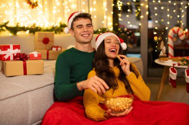 Mutlu karı koca Xmas filmi izliyor ve patlamış mısır yiyor. Yeni yıl şenlikli iç dekorasyonlarıyla örtülü olarak oturuyorlar.