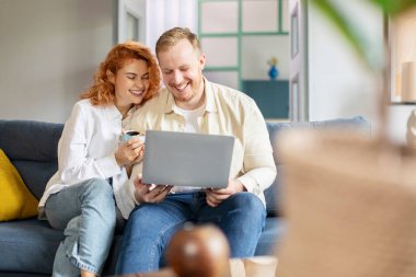 Genç Avrupalı çift kahve içip dizüstü bilgisayara bakıyor, internetten alışveriş yapıyor ya da evdeki kanepede otururken film arıyor.